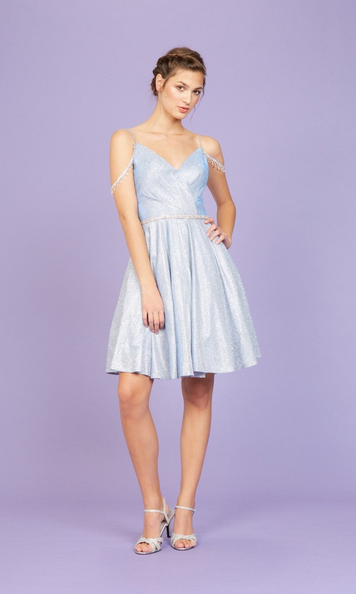 A woman poses against a light purple background wearing the Eureka 9722 Short Prom Dress in silver, paired with silver high-heeled sandals.